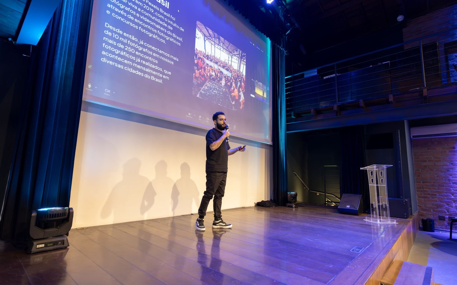 An adult speaker on a conference stage mid-presentation, a slide behind them showing the text of an open-source licence clause, the audience partially visible in the foreground
