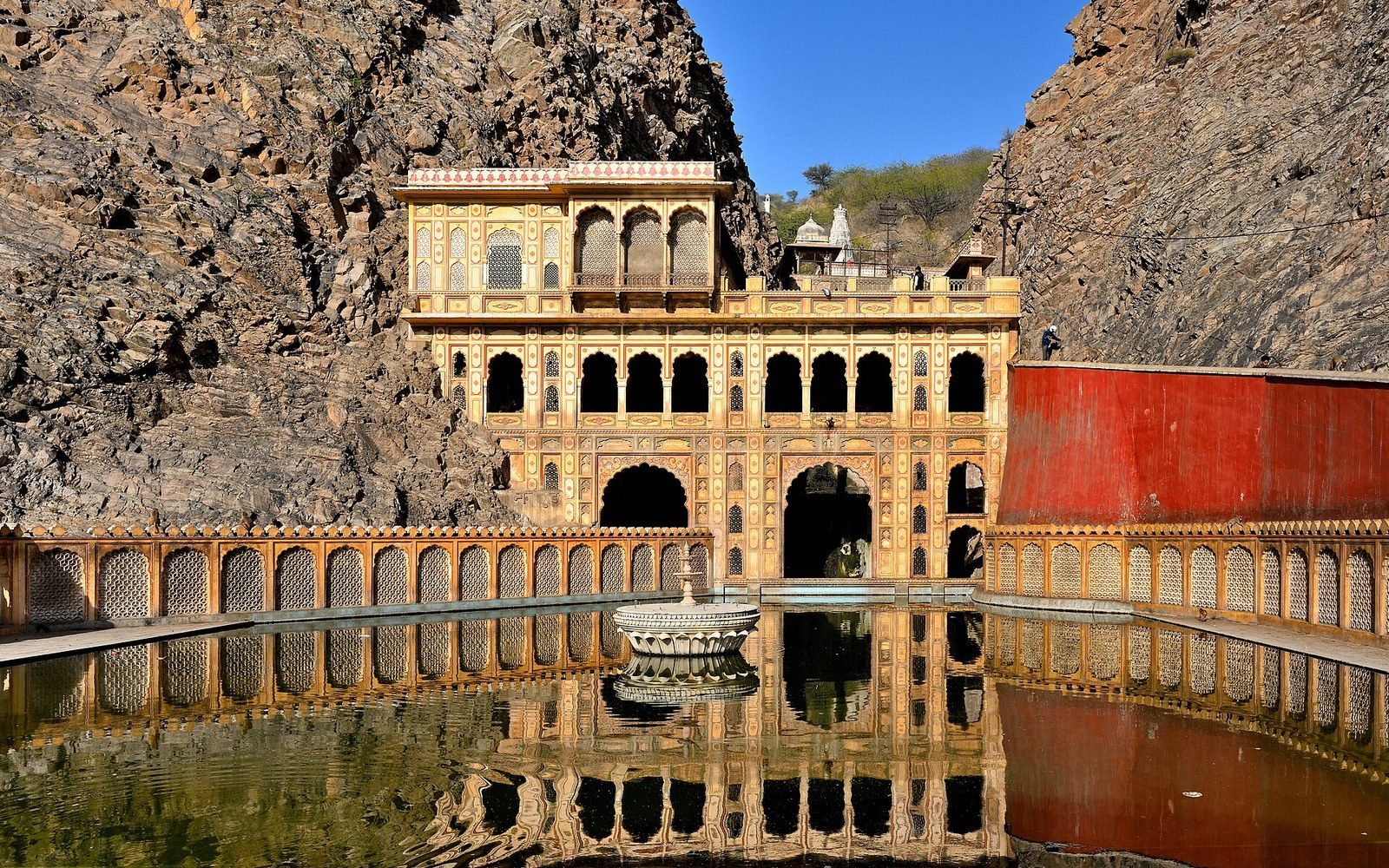 Arched temple facade with reflecting pool nestled between rocky cliffs