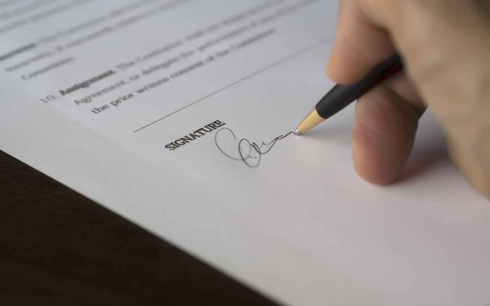 A hand signs a contract on the line marked "signature" with a pen