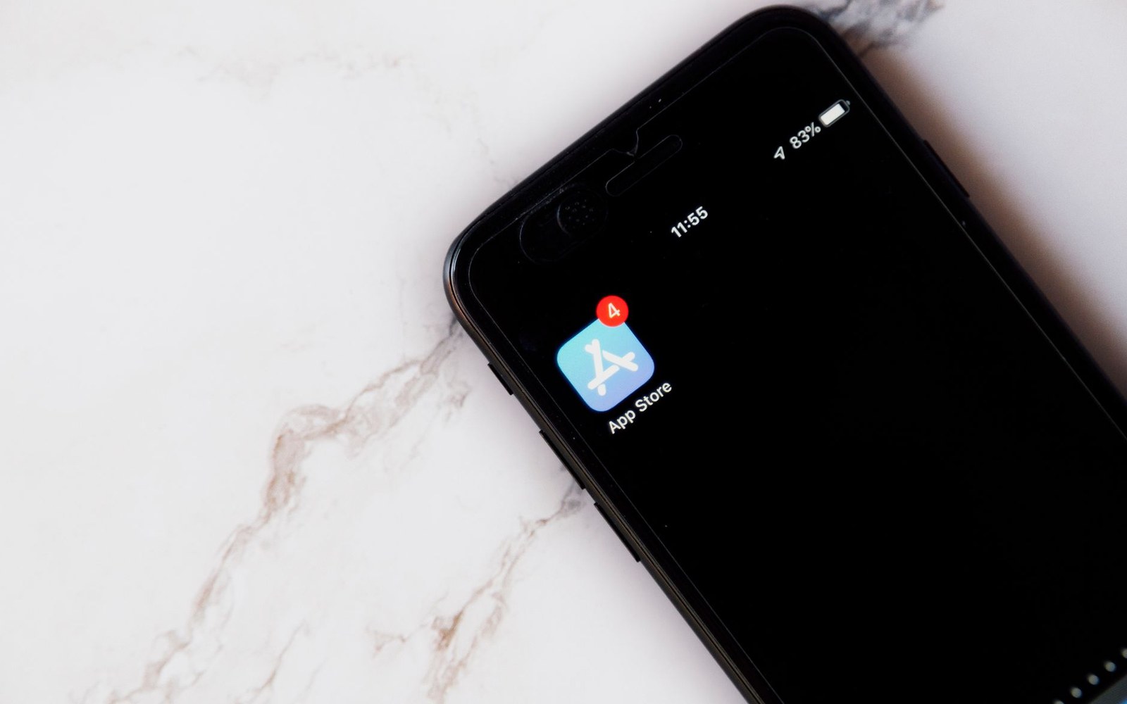 Smartphone screen showing the App Store icon with four notification badges, resting on marble