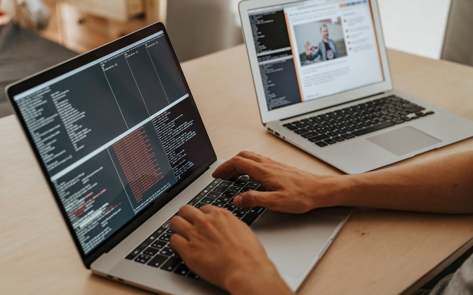 Hands typing code on a laptop with a second laptop showing a video call nearby