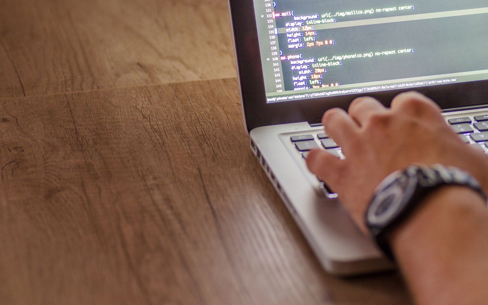 A hand types on a laptop keyboard displaying CSS code on the screen