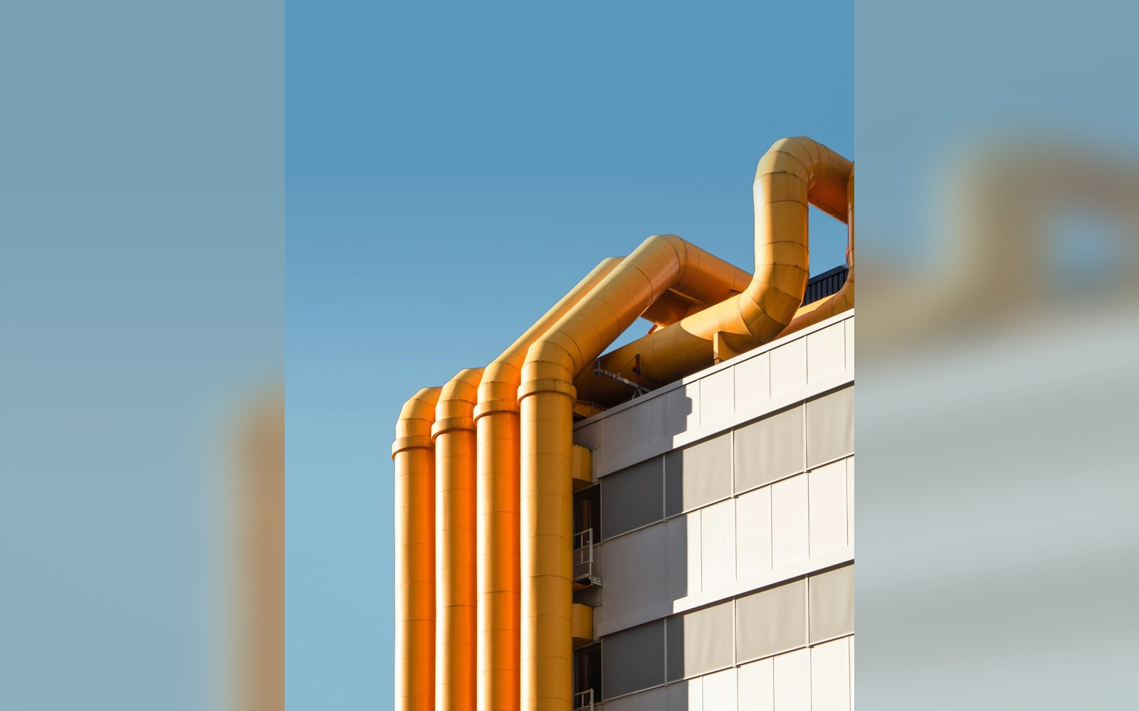 Large yellow exhaust pipes curve along the corner of a modern building