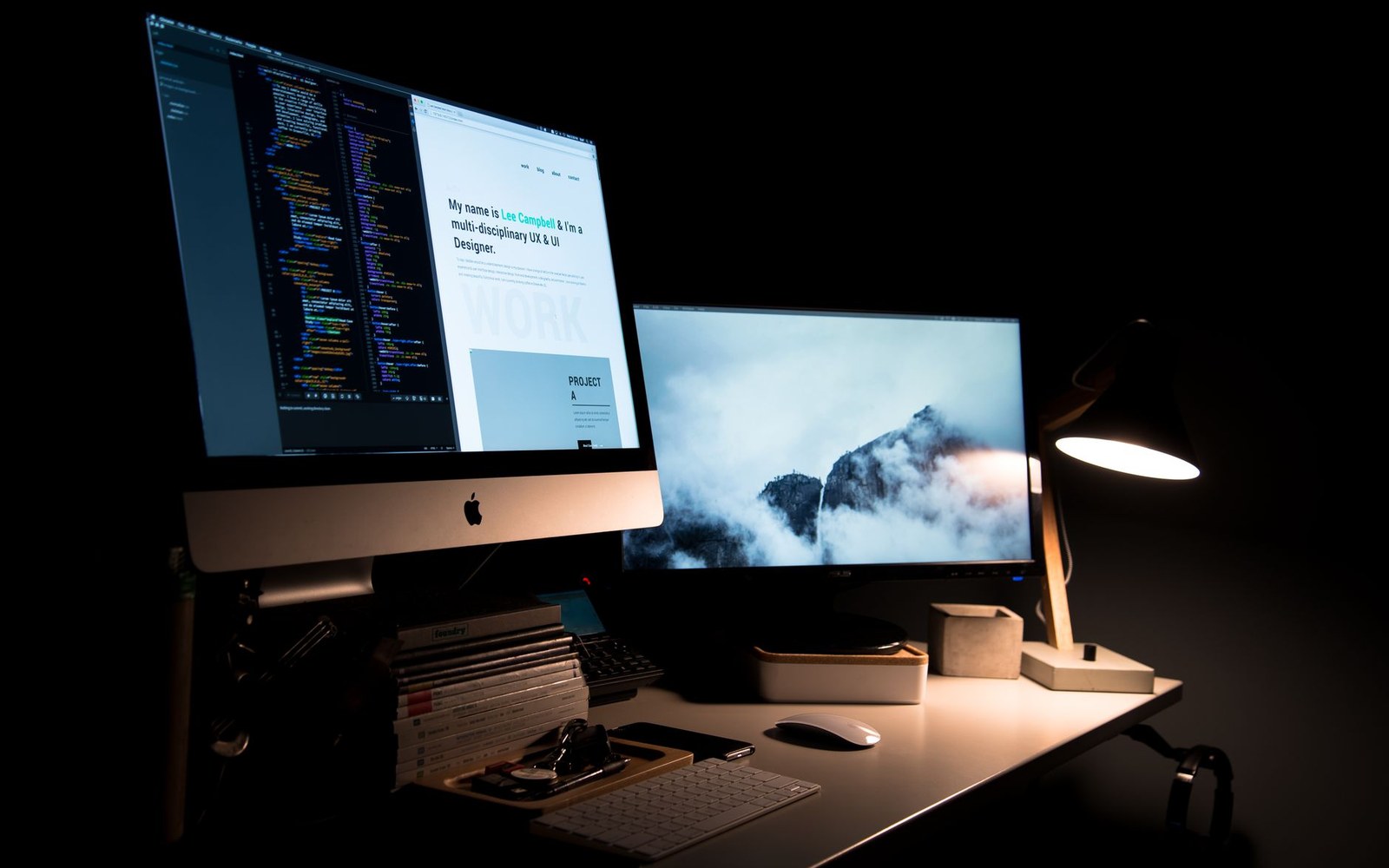 An adult developer's desk with two monitors showing a GitHub pull-request diff and a dependency graph, a coffee cup in the foreground, shot in available office light