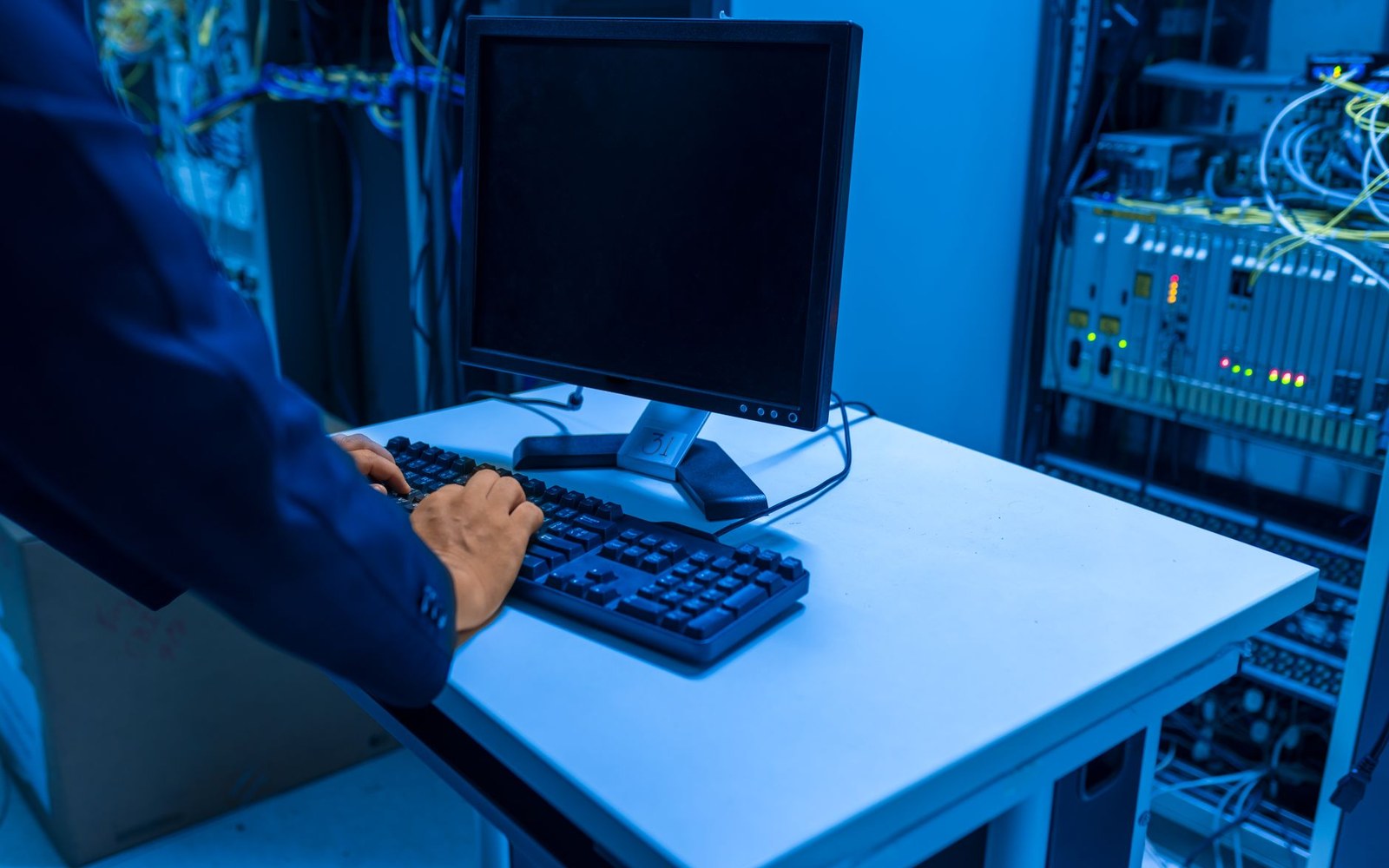 A long aisle of server racks in a data centre, one door open with a technician's hand visible